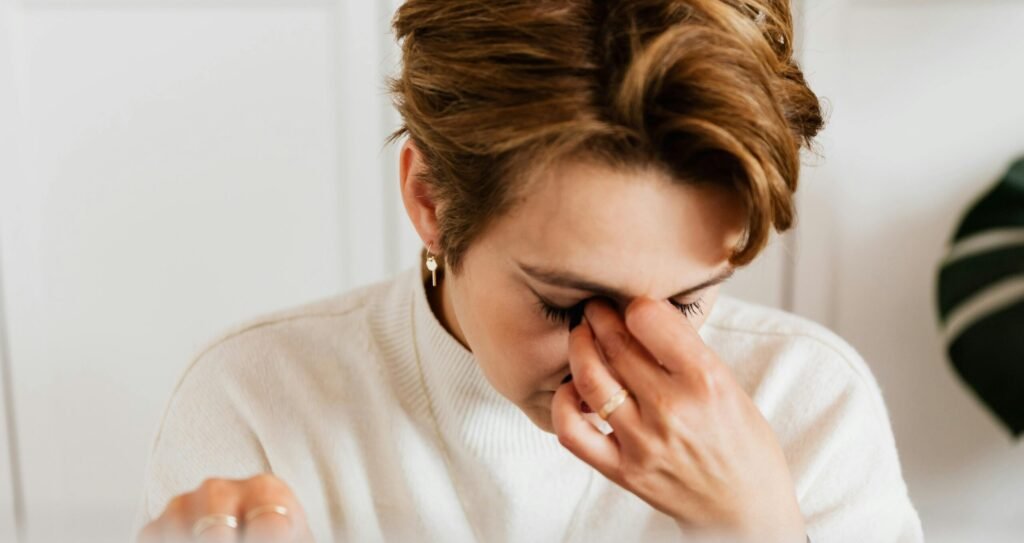 A close-up shot of a woman rubbing her eyes, conveying stress and fatigue indoors.